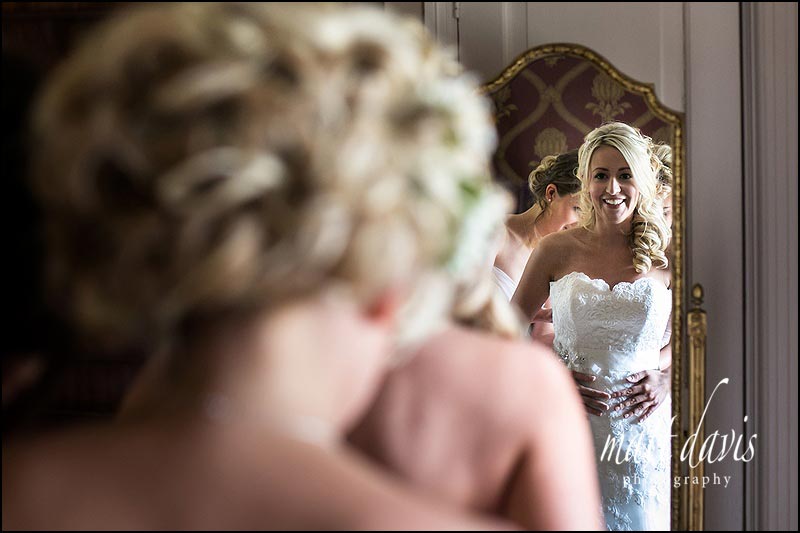 Bride smiling in mirror as she puts on her wedding dress
