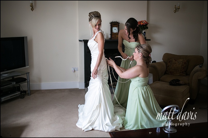 Bride having wedding dress tied at the back by bridesmaids in sage green dresses