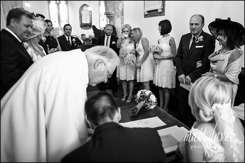 black and white documentary photography of signing of the wedding register at Kingscote Church, Gloucestershire
