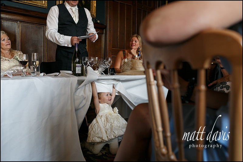 Documentary wedding photography.  Bridesmaid hiding under table during wedding speeches